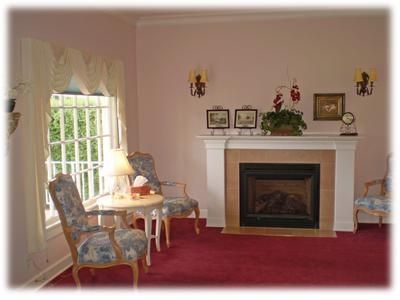 Cozy living room with red carpet, fireplace mantel, armchairs, and a window with a lamp beside it