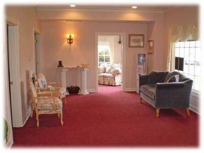 Living room with red carpet, fireplace, armchairs, sofa, and a doorway to a bright bedroom