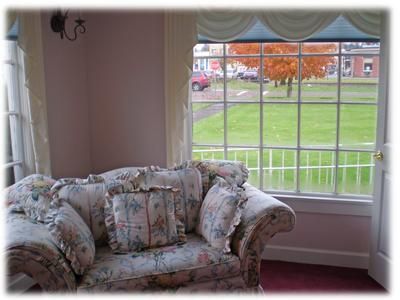 Floral sofa by a large window overlooking a green lawn and autumn trees