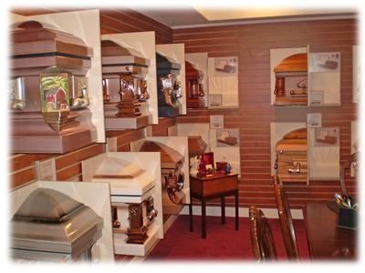 Small room with lined wooden caskets and urns displayed on shelves and tables