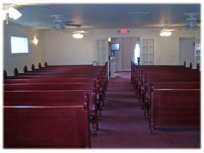 Empty church sanctuary with wooden pews, purple carpet, and ceiling lights leading to the front door