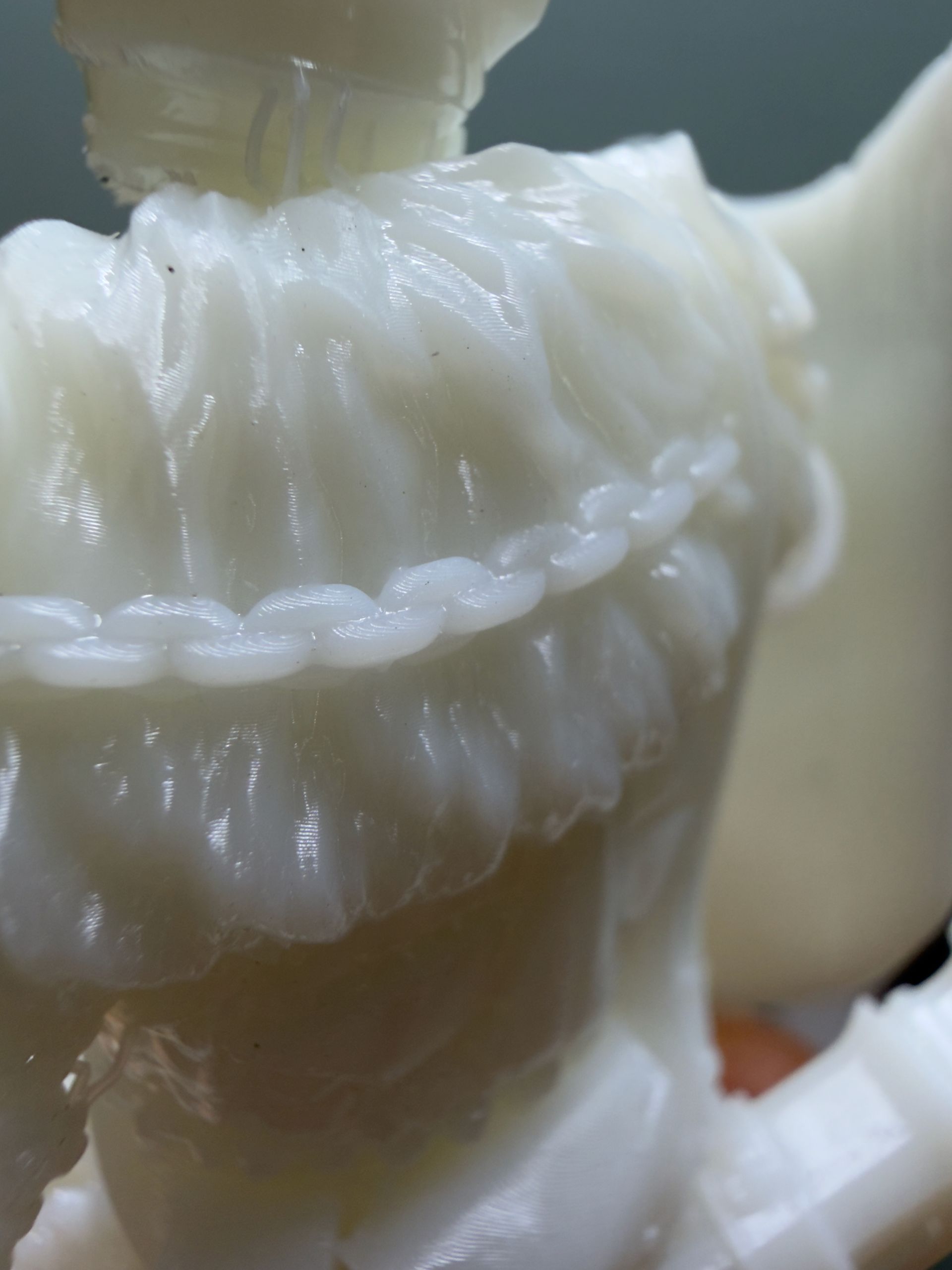 A close-up view of a white, 3D-printed figurine featuring a detailed chain accent draped over textured, layered armor.