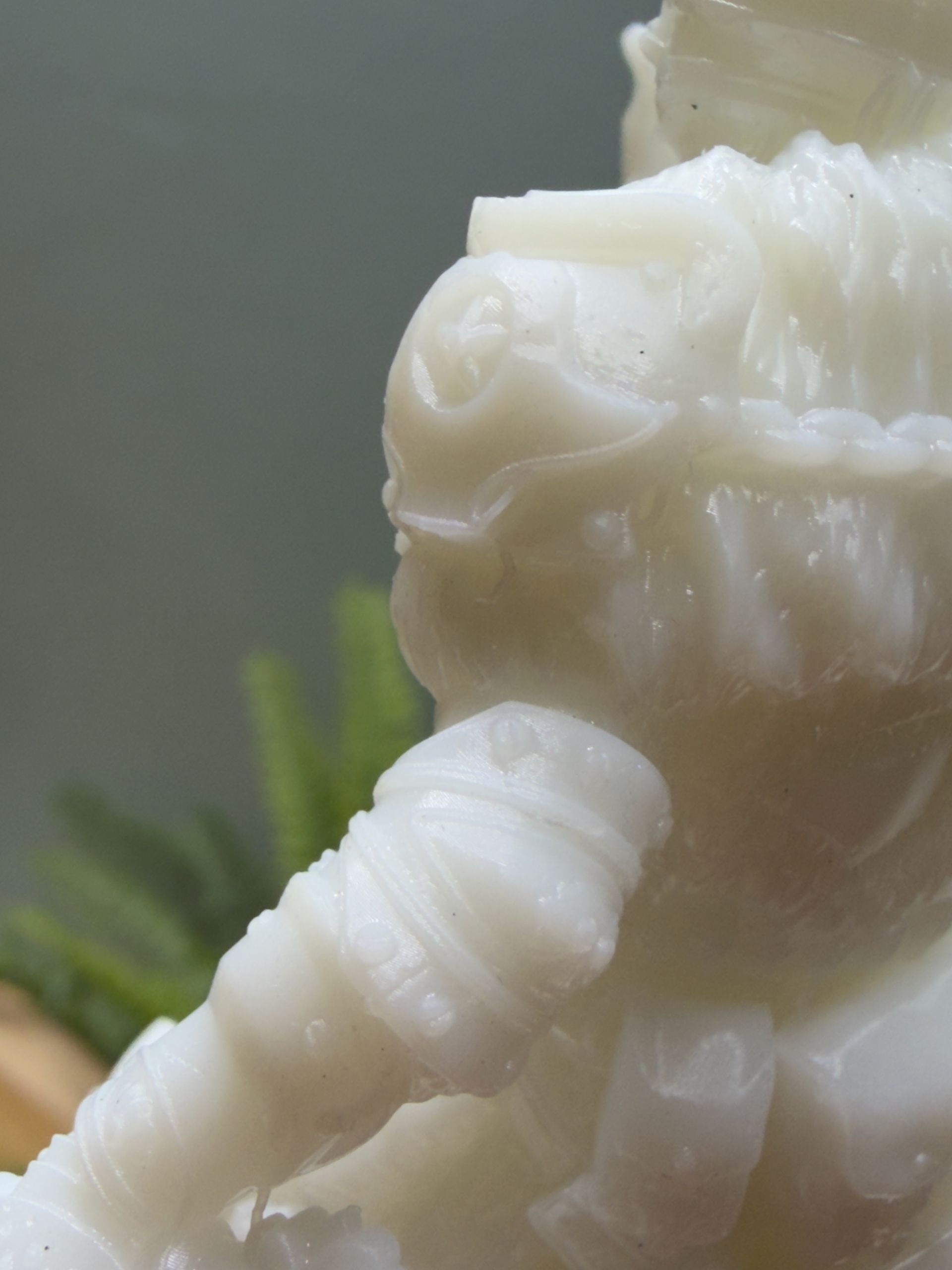 Close-up of a white, carved stone figurine depicting a warrior in armor, set against a blurry green background.