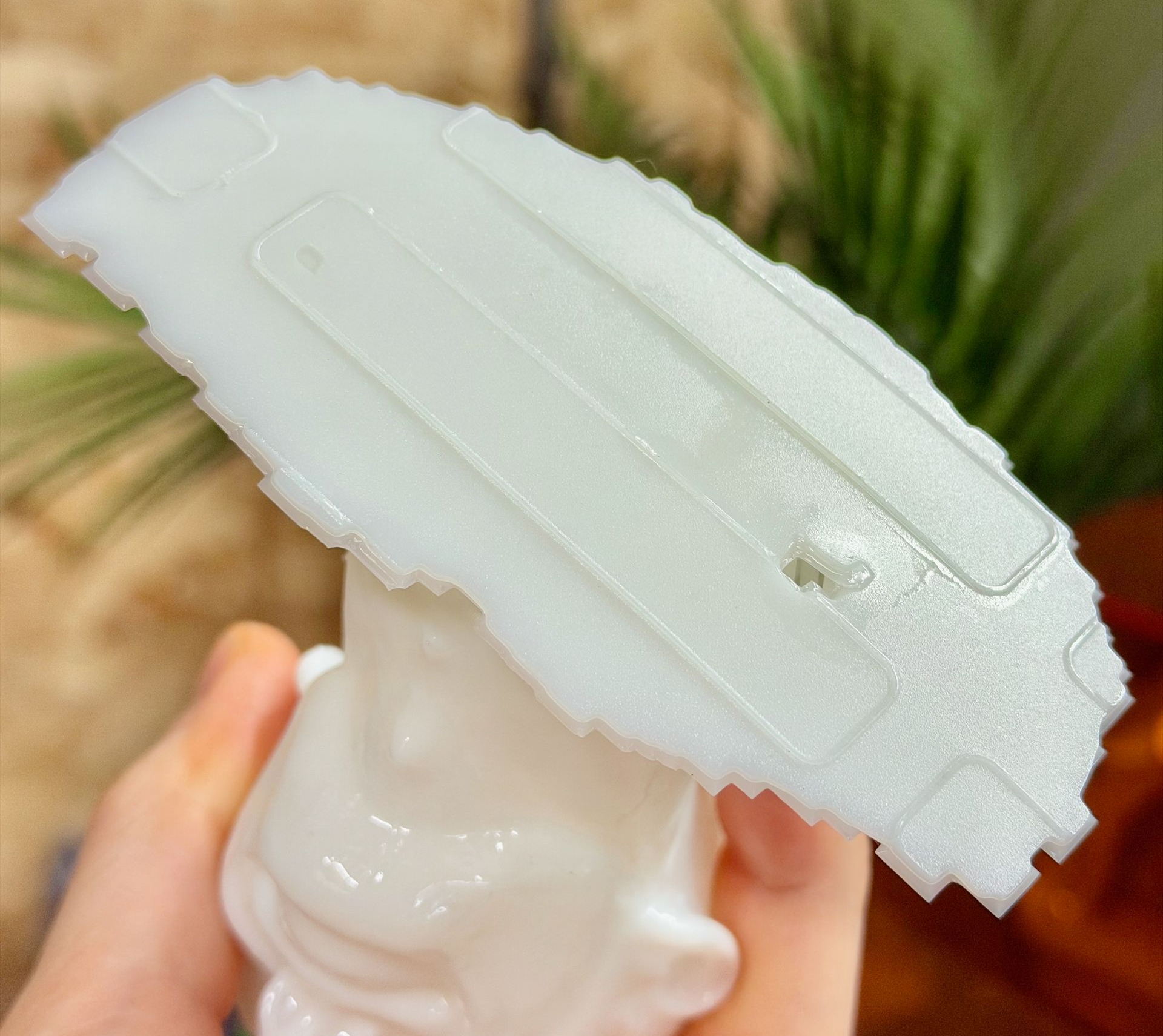 A hand holds a translucent white, textured, shield-like object above a smooth white sculpted head.
