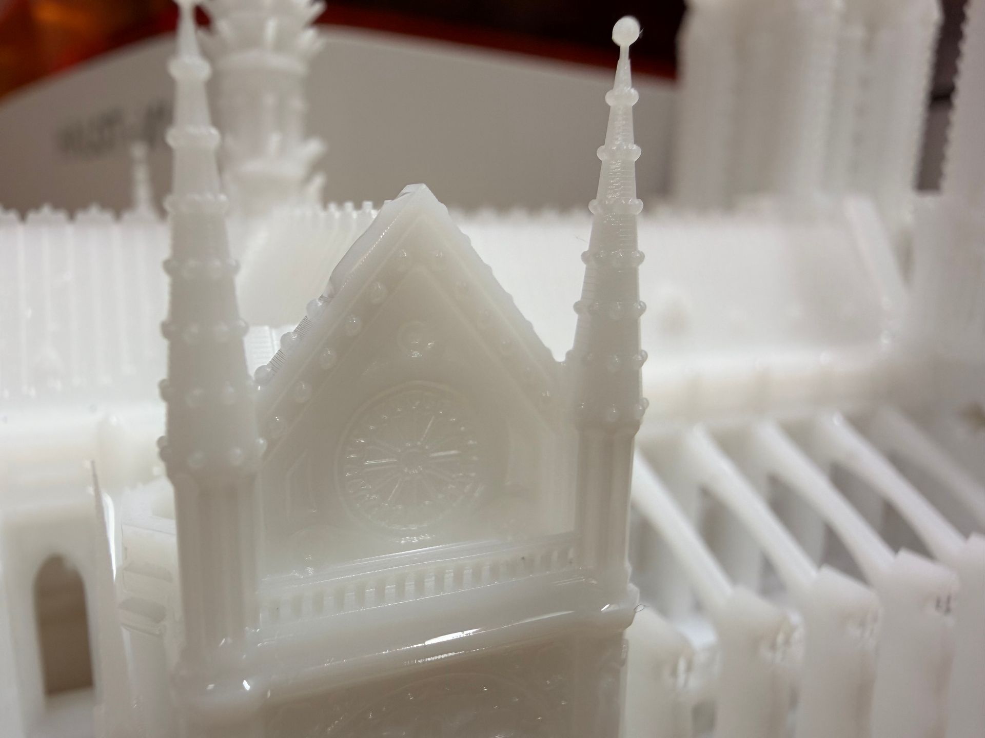 A white 3D-printed miniature model of a Gothic cathedral, featuring a rose window, pointed gables, and decorative spires.