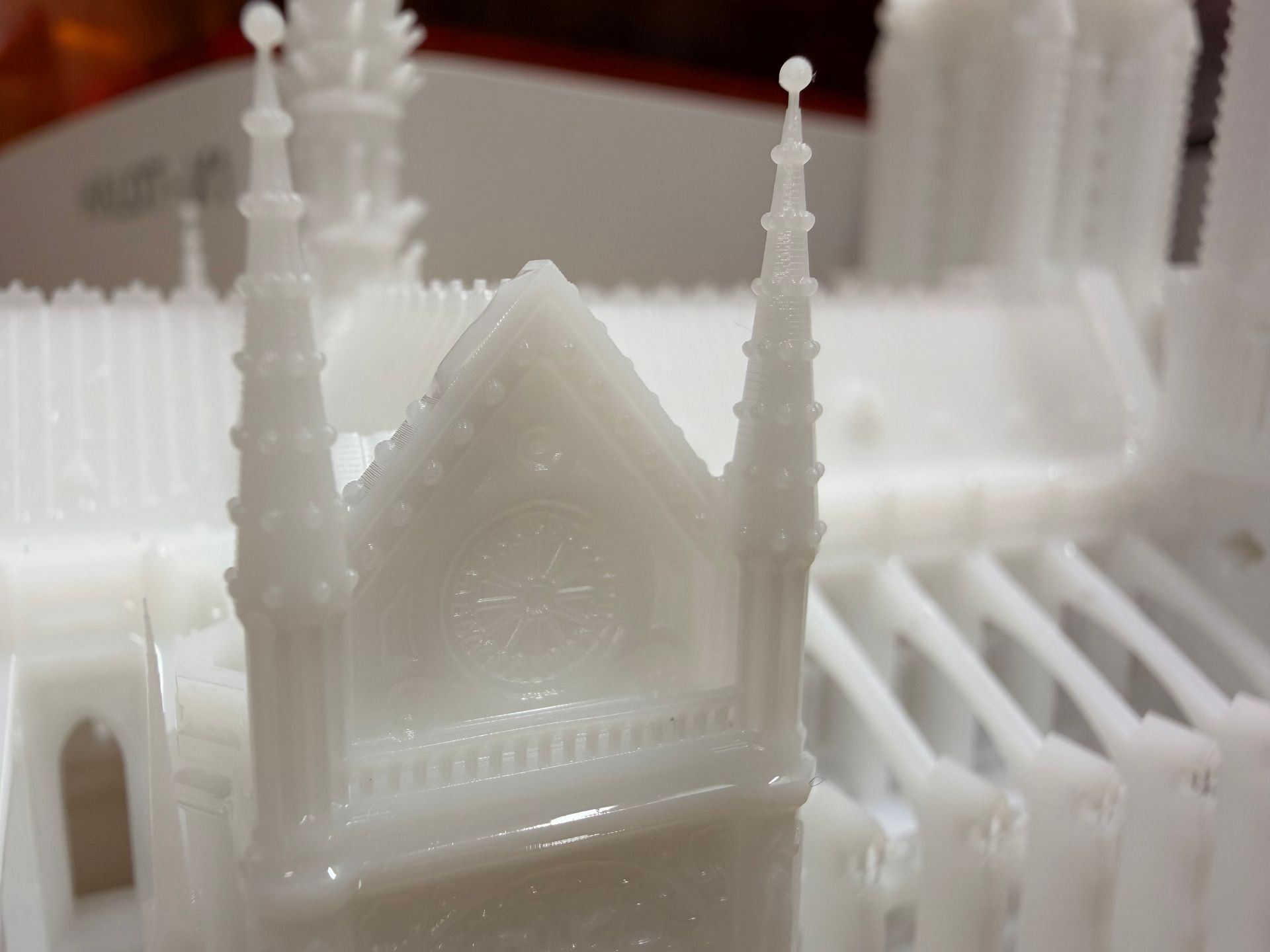 A detailed, unpainted white 3D-printed model of a Gothic cathedral's spire and roof section.