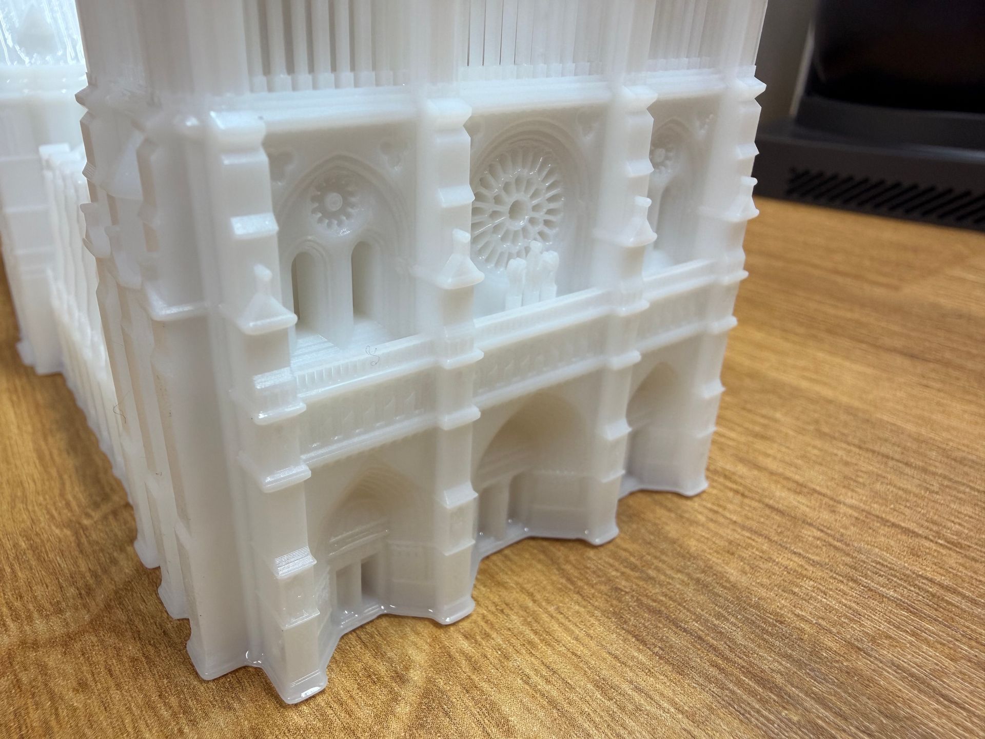 A white 3D-printed miniature model of a Gothic-style cathedral resting on a wooden surface.