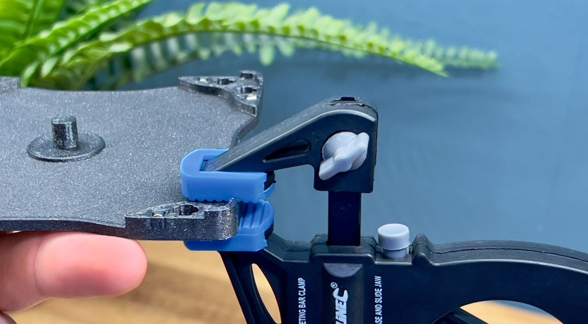 A close-up view of a hand using a black and blue clamp tool to secure a textured, grey plate.