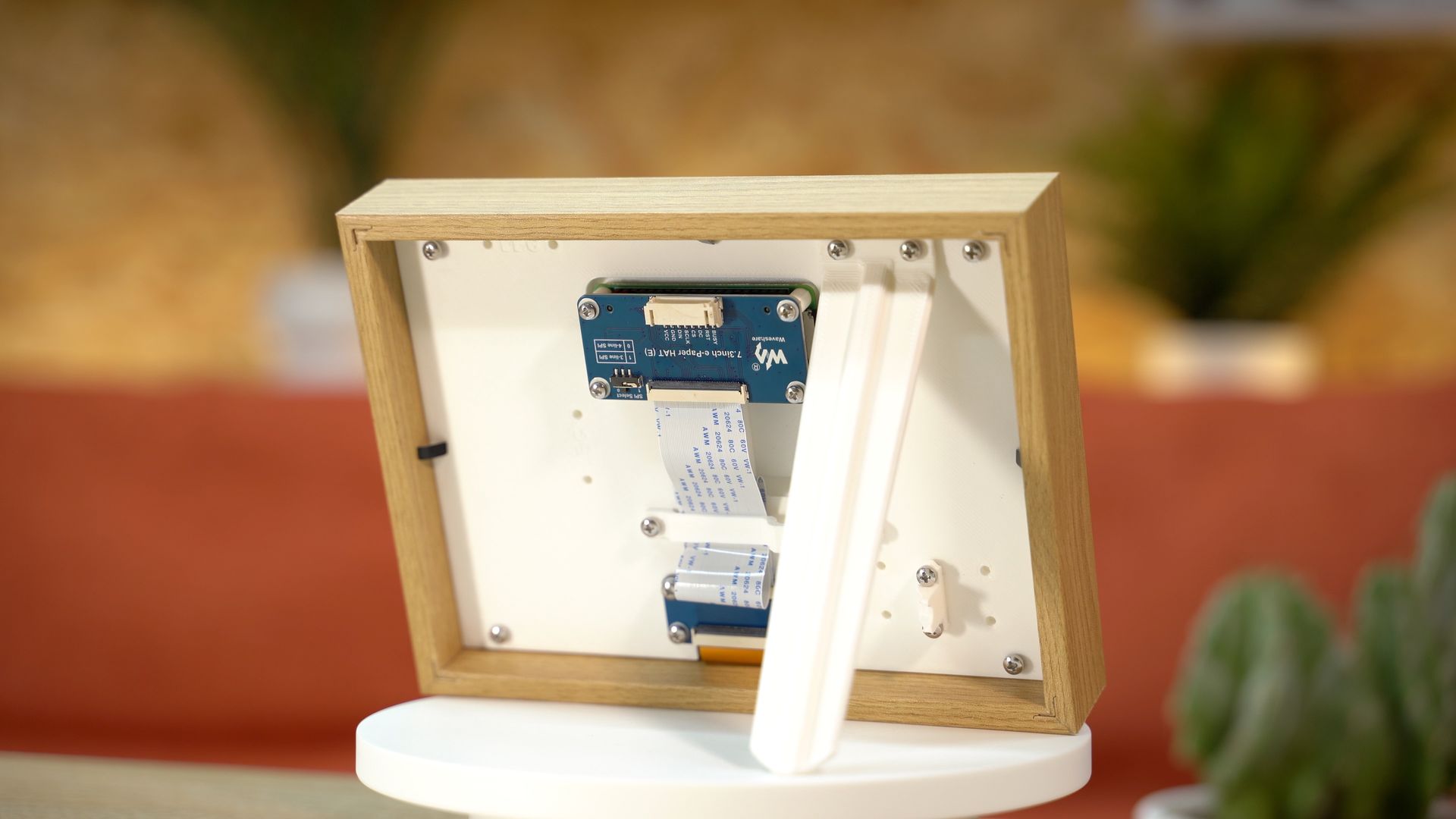 The back of a wooden picture frame revealing electronic components, including blue circuit boards connected by ribbon cables.