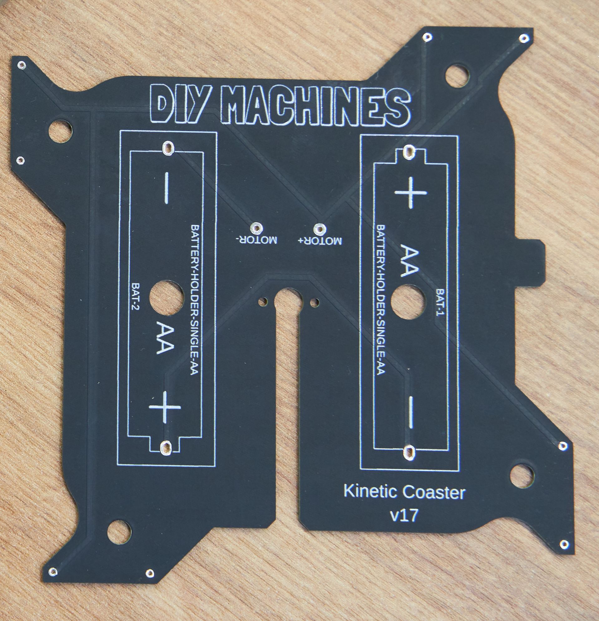 Black custom circuit board for a DIY Machines Kinetic Coaster, featuring two AA battery holders and motor connection ports.