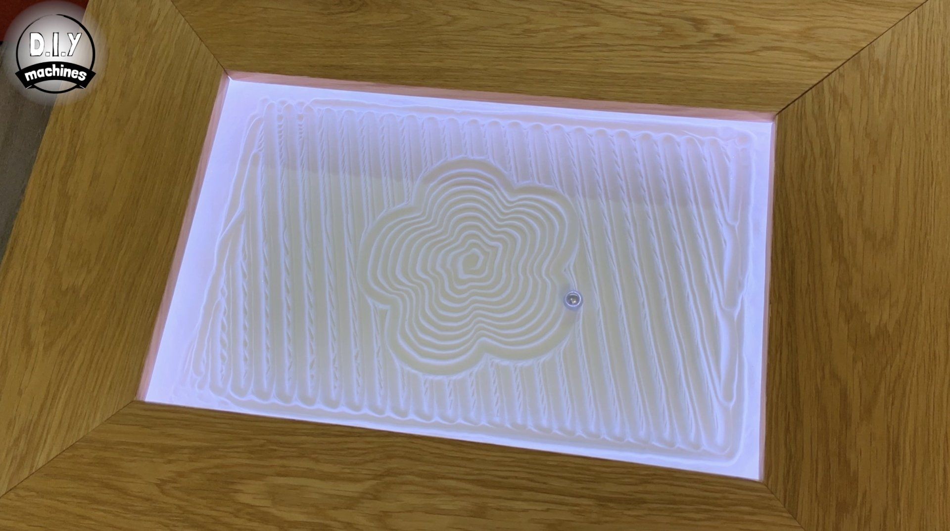 A wooden-framed sand table features a decorative, circular flower pattern traced into the white sand.