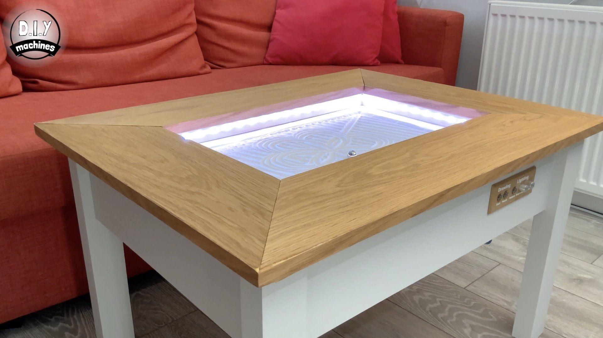 A white coffee table with a light-up glass center panel featuring blue LED lighting, set in front of an orange sofa.