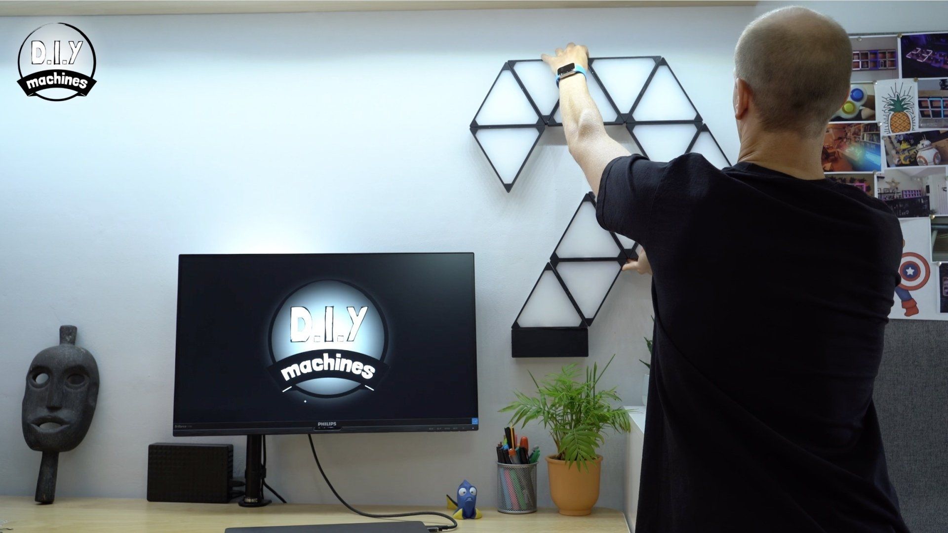 A person mounting geometric wall lights above a computer monitor on a desk.