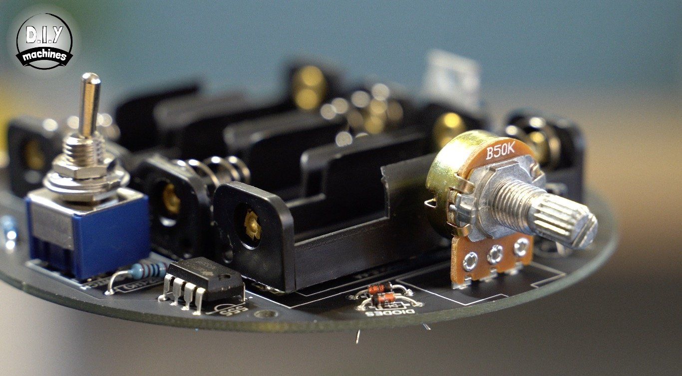 A circular electronic circuit board featuring a battery holder, a toggle switch, and a rotary potentiometer.