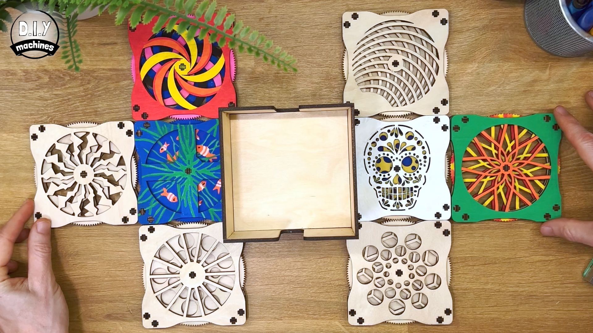 A wooden box unfolds to reveal colorful panels featuring various laser-cut mandala and sugar skull patterns on a table.