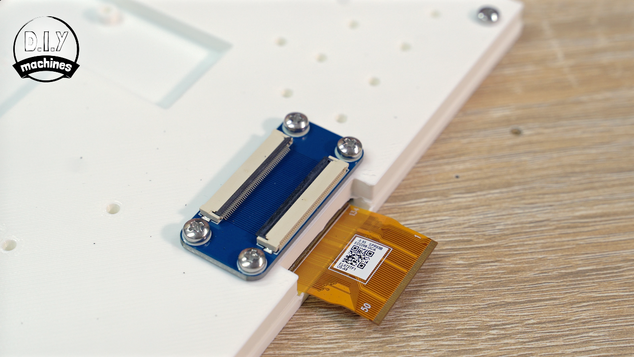 A small blue circuit board with two FPC connectors screwed onto a white surface, connected to a flexible gold ribbon cable.