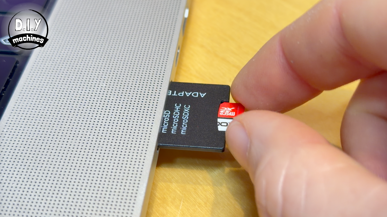 A hand inserts an SD card adapter into the side slot of a laptop.