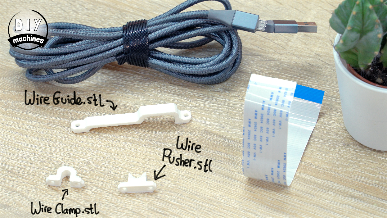 3D-printed wire components: a guide, clamp, and pusher, arranged with a gray USB cable and a flat ribbon cable.