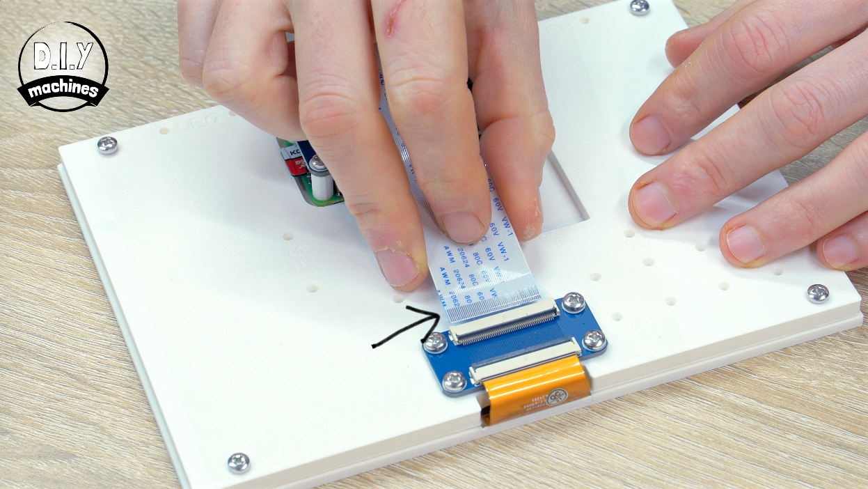 Hands insert a flat ribbon cable into a blue electronic connector on a white panel.