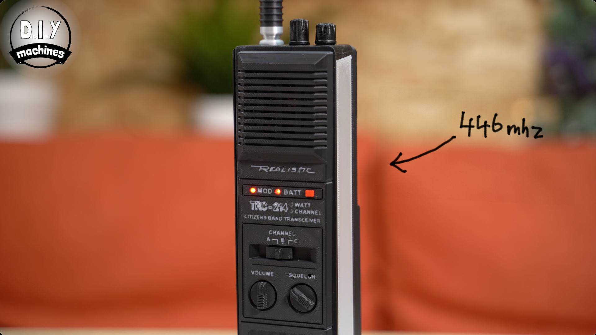 A handheld black walkie-talkie standing on a table, with a hand-drawn arrow pointing to it labeled