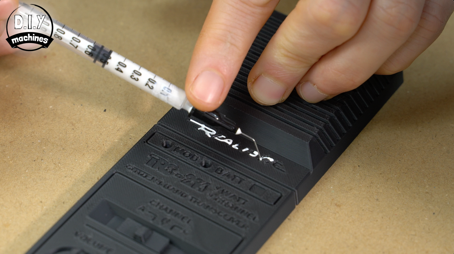 A syringe applies white thermal paste to the processor chip on a black rectangular heatsink.