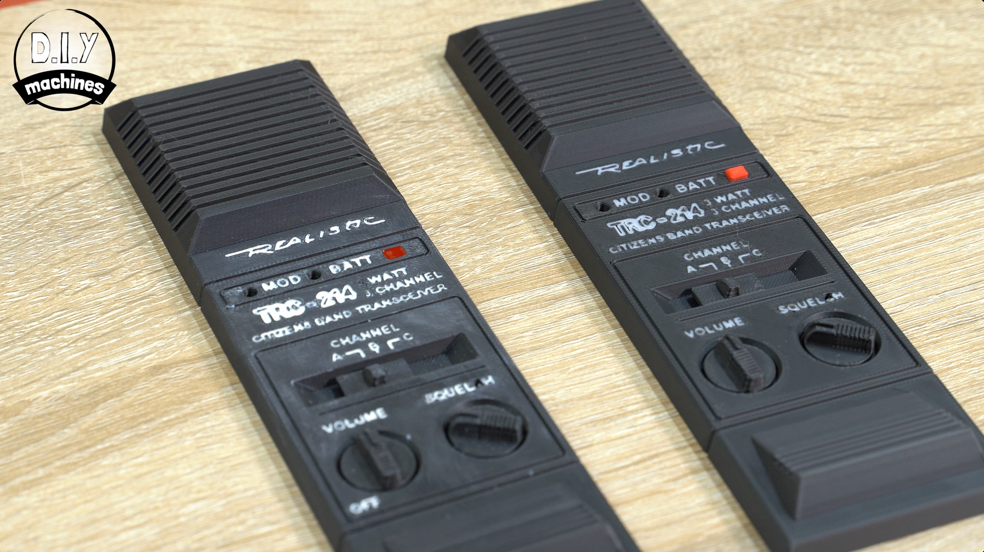 Two black, vertical handheld transceivers or walkie-talkies with volume and power knobs resting on a wooden surface.