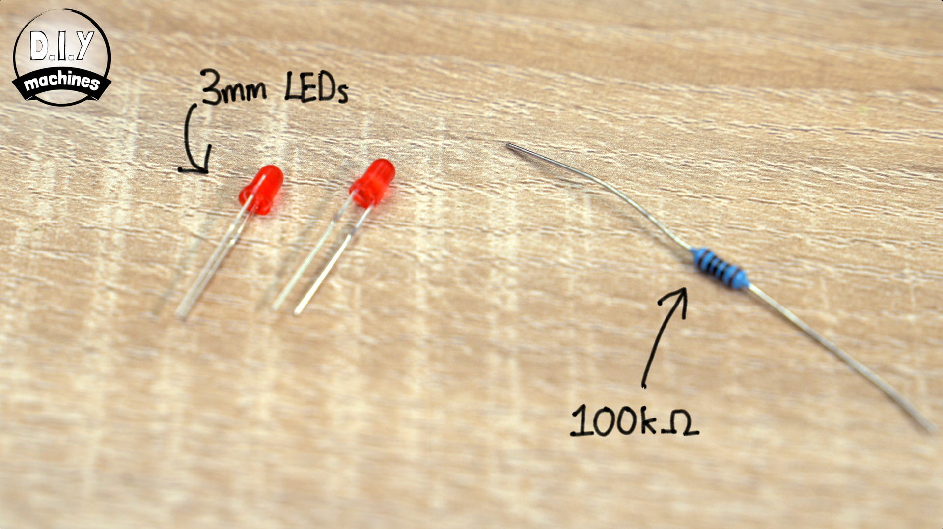 Two small red 3mm LEDs and one blue-banded 100kΩ resistor lying on a wooden surface.
