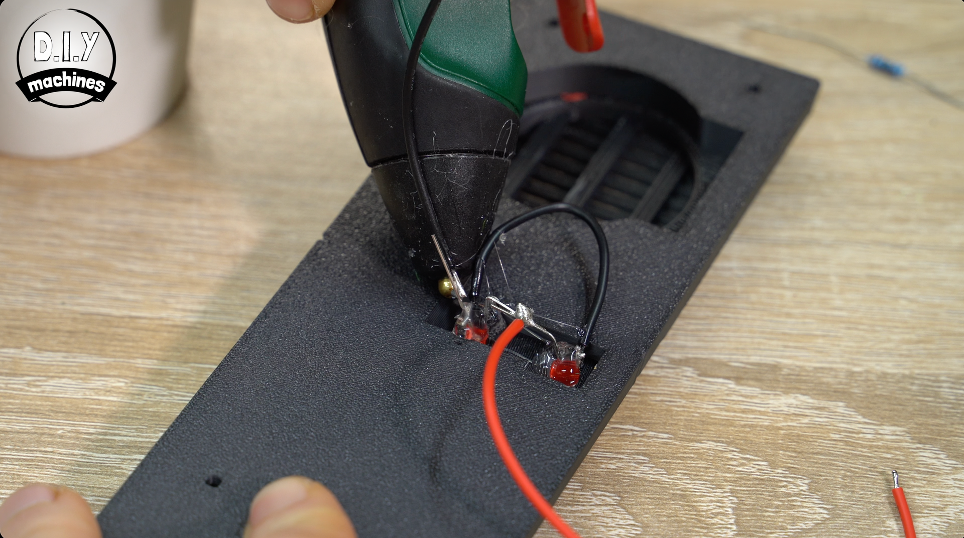 A hot glue gun is used to secure small LED components into a textured black panel during an electronics project.