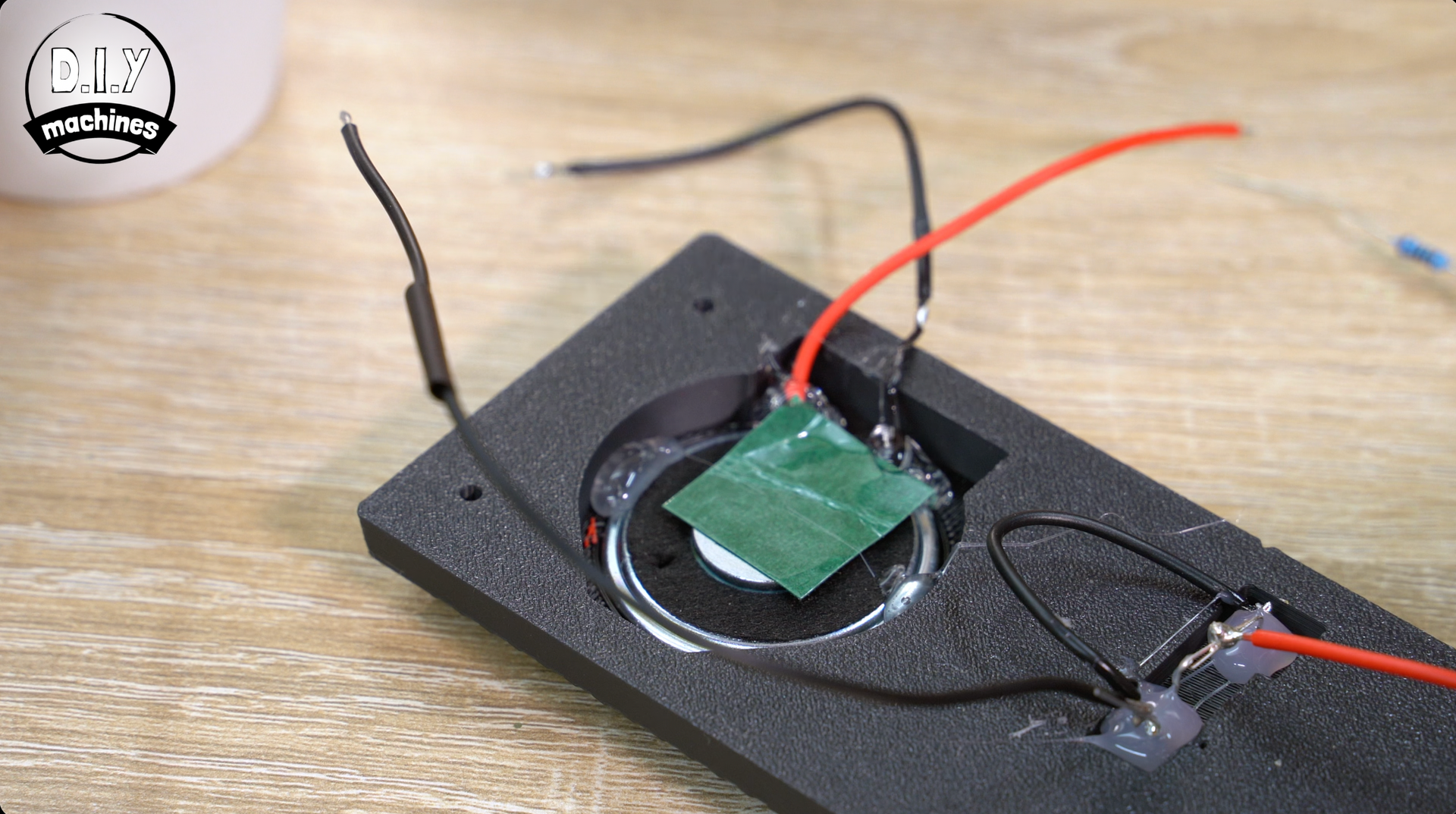 An electronic component with black and red wires is embedded in a black foam base, showing a green square circuit part.
