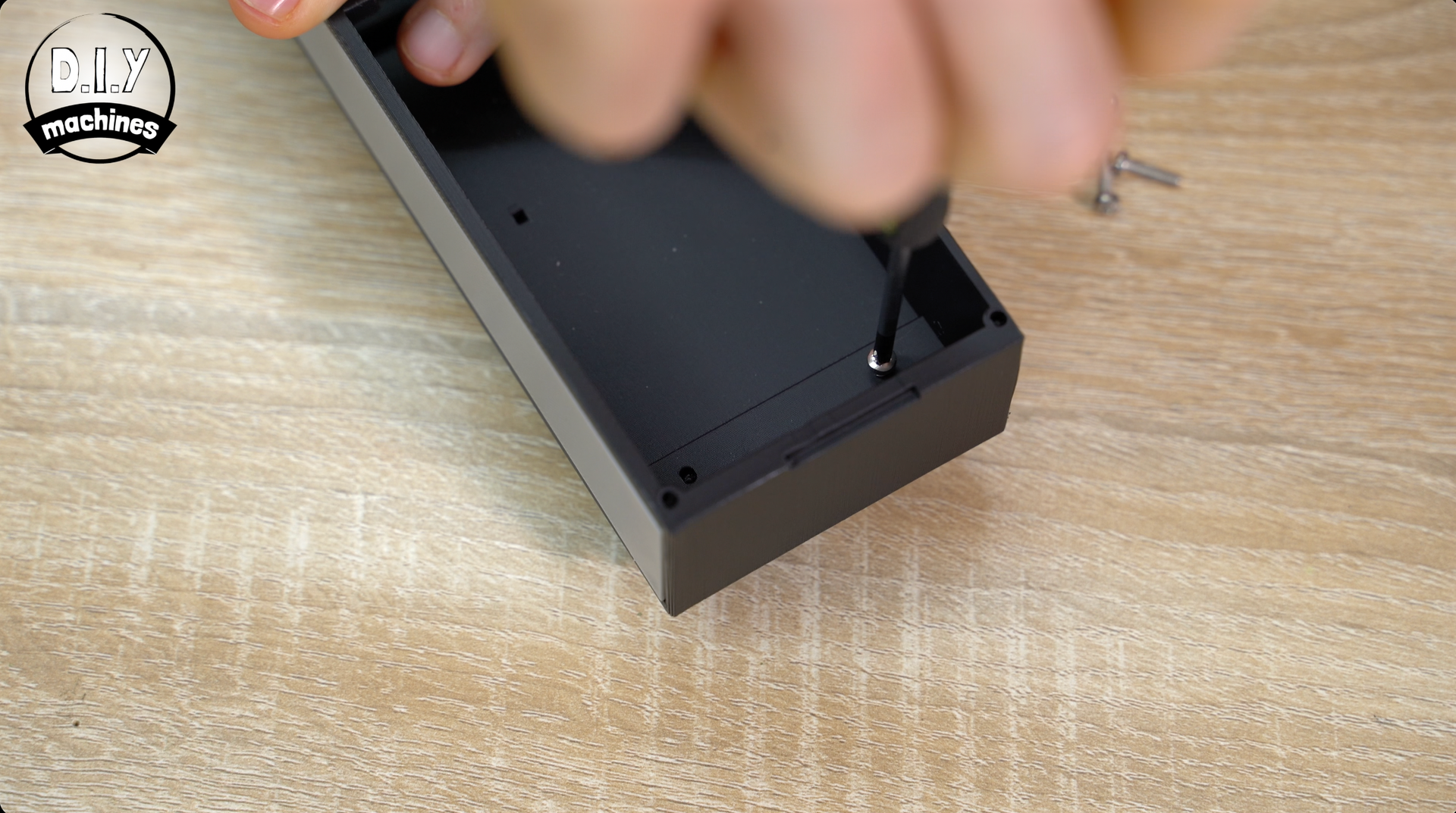 A person uses a screwdriver to secure a screw into the interior corner of a black rectangular electronics case.