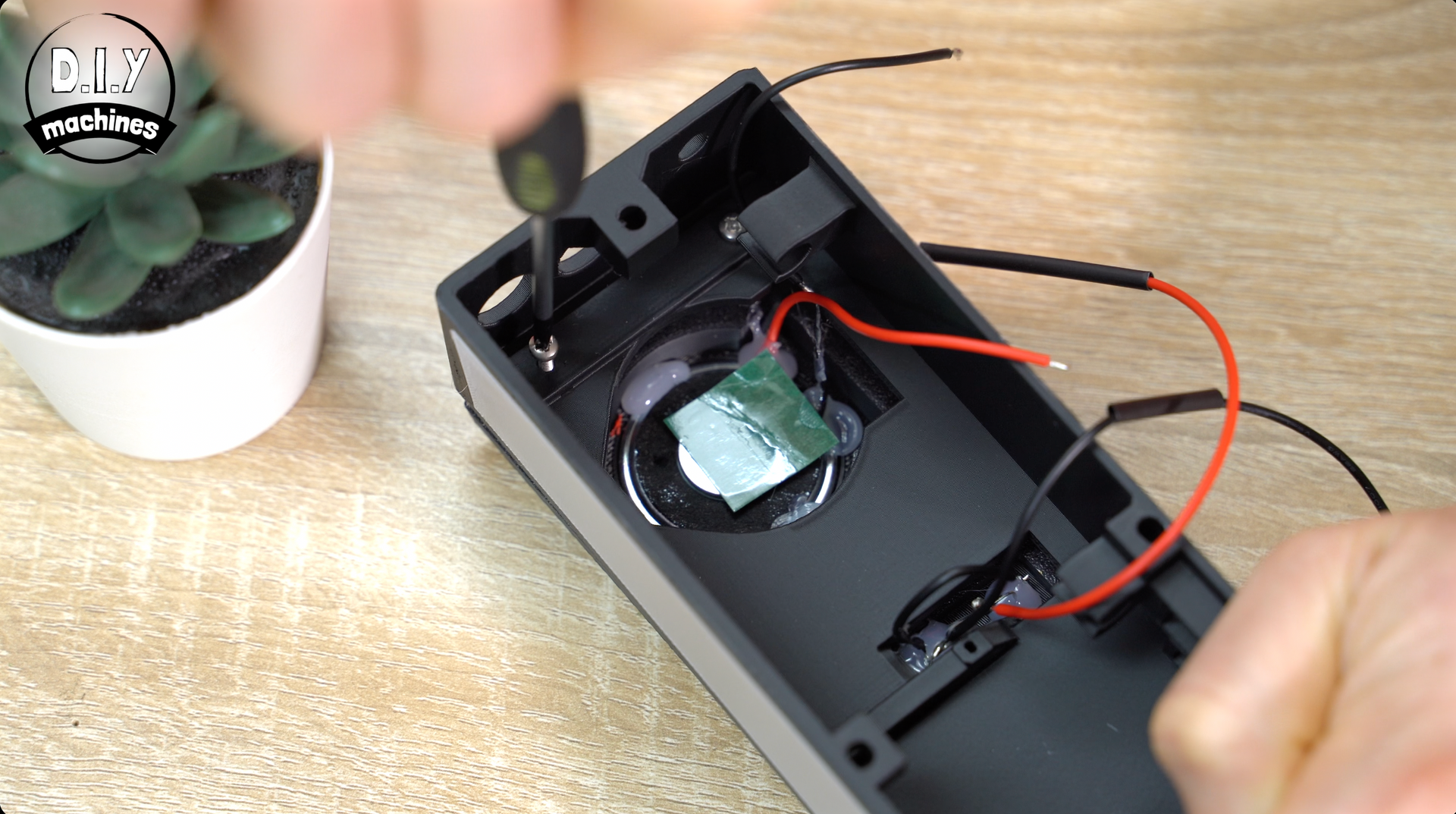 A person uses a screwdriver to secure a component inside the black housing of a small electronic device.
