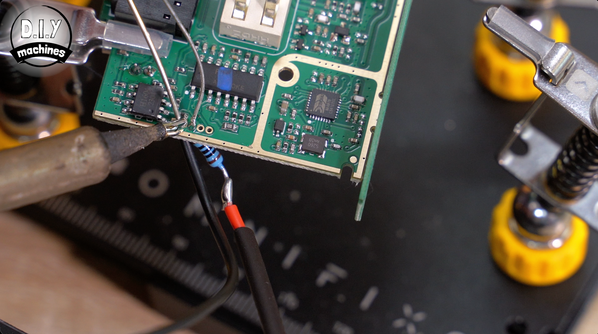 A soldering iron point touches a circuit board component, connecting a wire with a blue resistor to a board terminal.