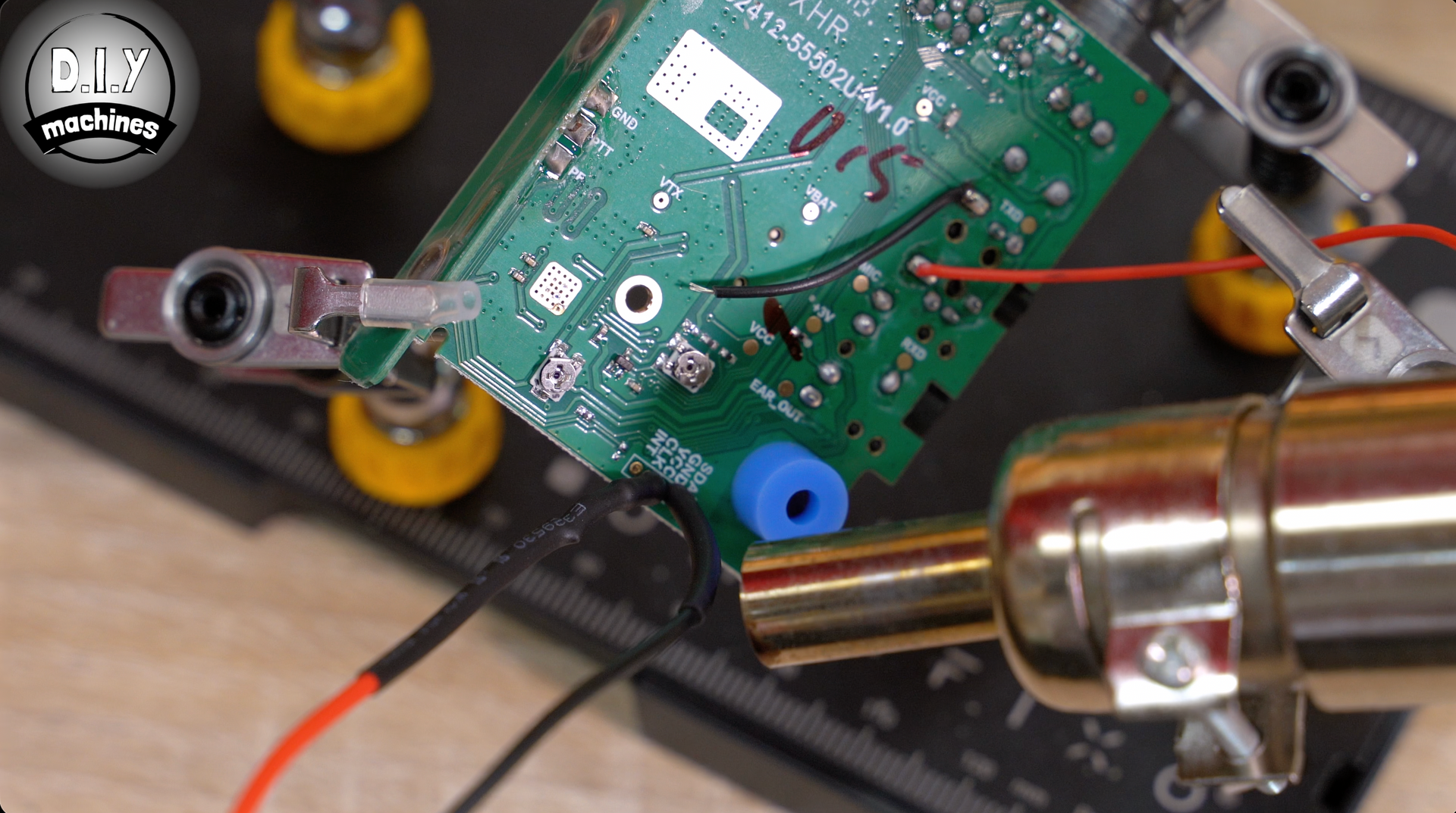 A hot air rework station is used to heat a connection on a green printed circuit board held by helping hand clips.