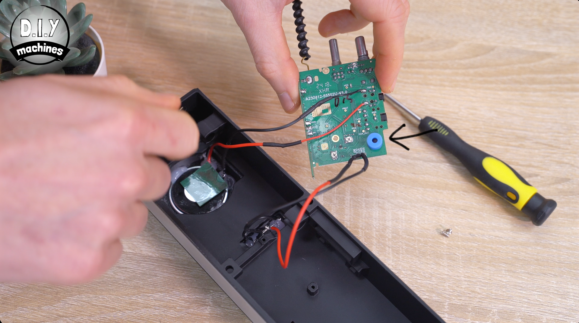 A person disassembles an electronic device, holding a circuit board with a small blue component near a screwdriver.