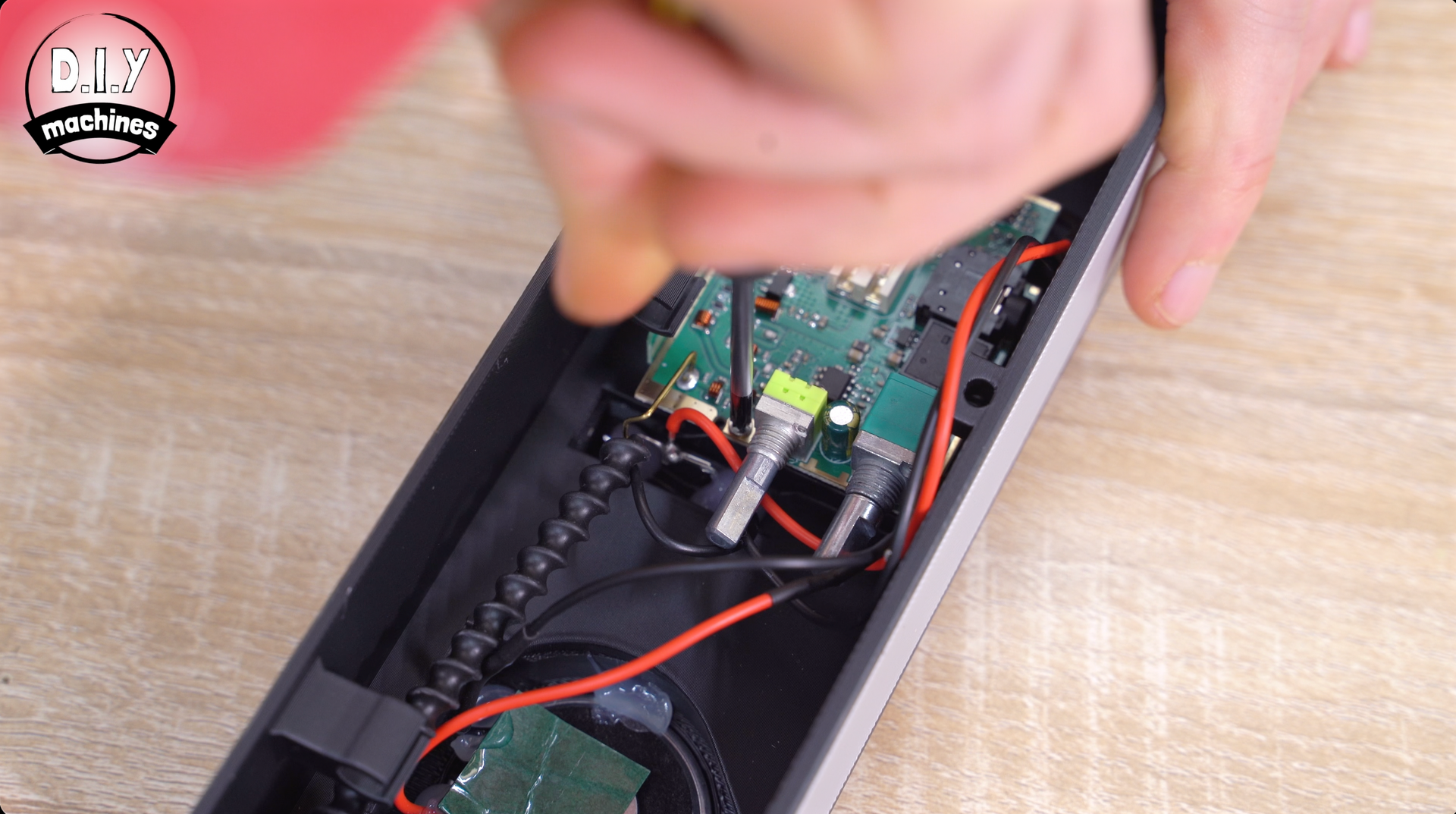 Hands using a screwdriver to disassemble the circuit board inside a black electronic device casing.