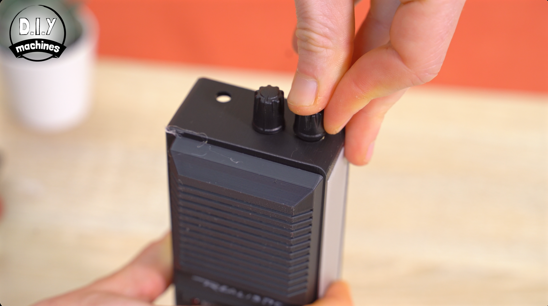 A person's hands adjust the black knob on top of a portable gray speaker or electronic device on a wooden surface.