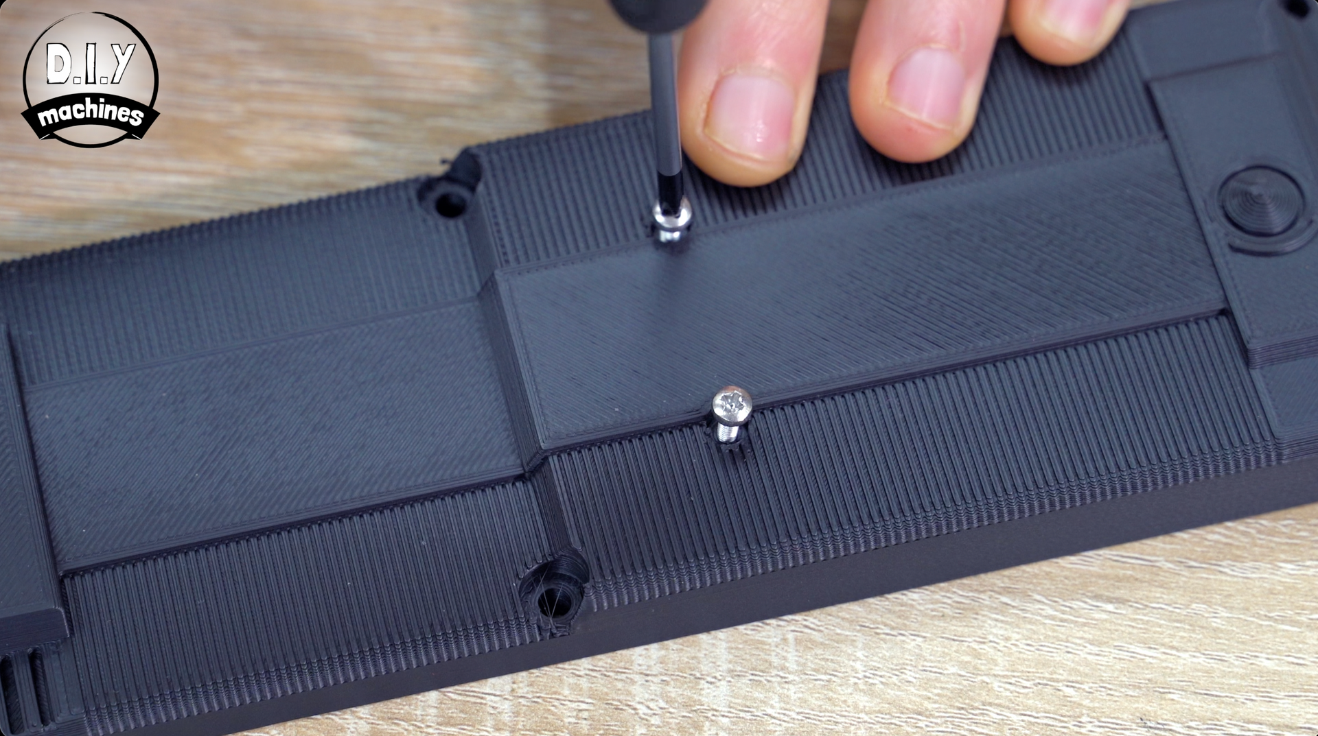 A screwdriver being used to secure a screw into a black, textured plastic component on a wooden surface.