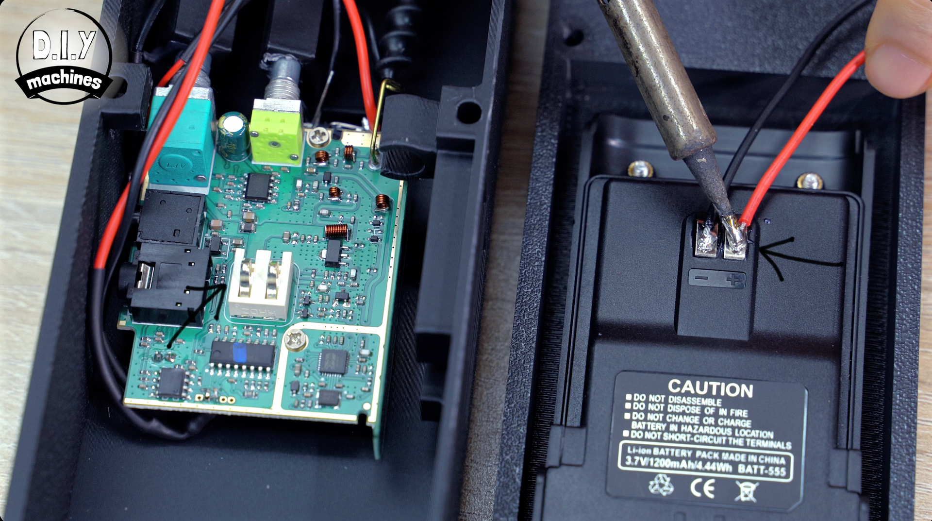 A person uses a soldering iron to attach red and black wires to the battery compartment of an open electronic device.