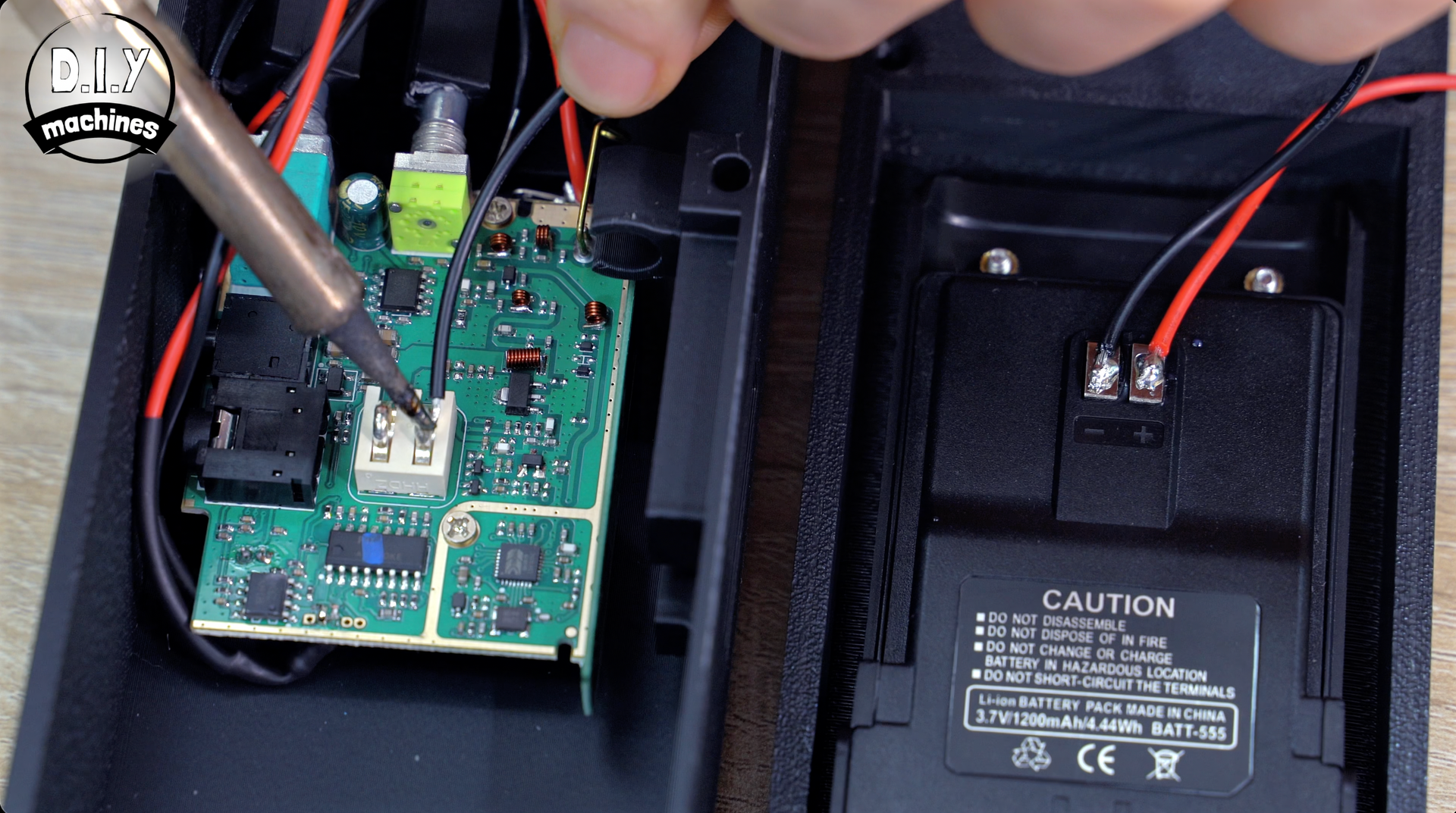 A hand uses a soldering iron to connect a wire to a circuit board inside an open electronic device.