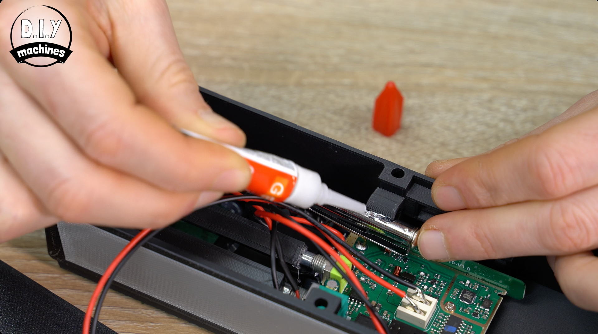 Hands apply adhesive from a small tube to a metal component inside a plastic electronic device housing.