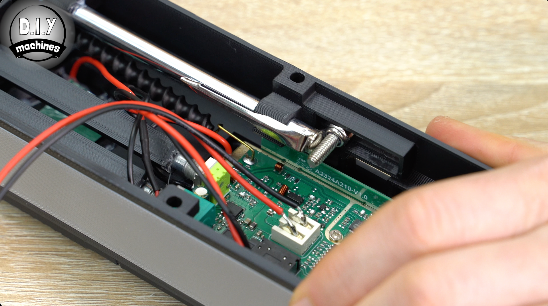 A hand reaches into an open electronic device housing, revealing a green circuit board with wired connections and an antenna.