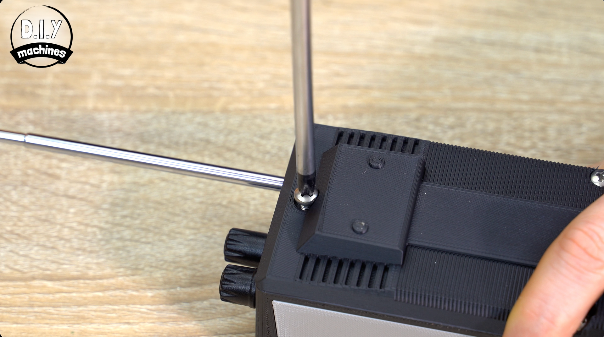 A hand uses a screwdriver to tighten a screw on the black casing of a portable electronic device.