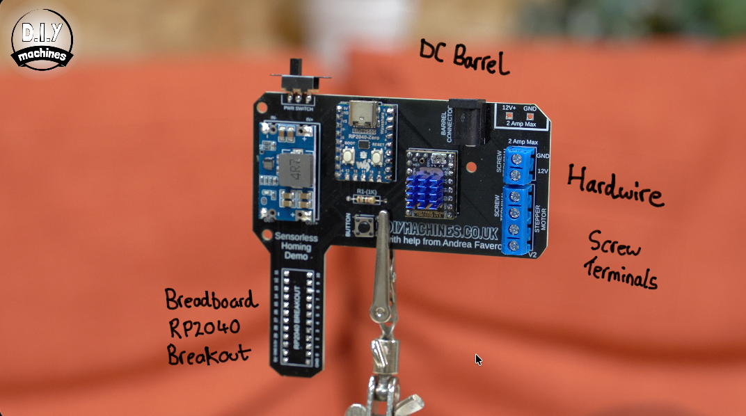 A circuit board mounted in a helping hand tool, featuring an RP2040 breakout, DC barrel jack, and blue screw terminals.