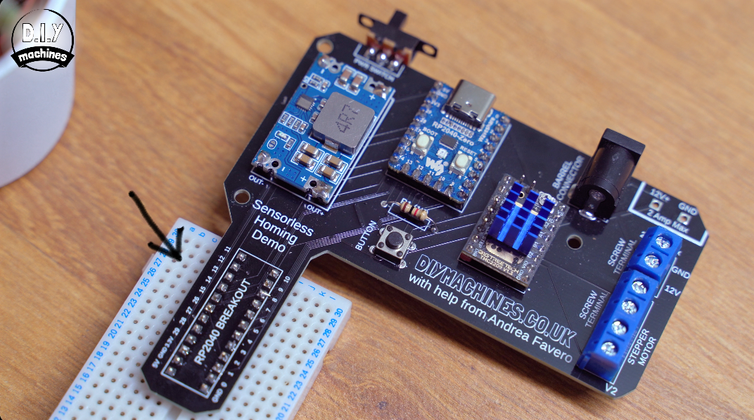 A black custom PCB board with electronic components plugged into a white breadboard on a wooden table.