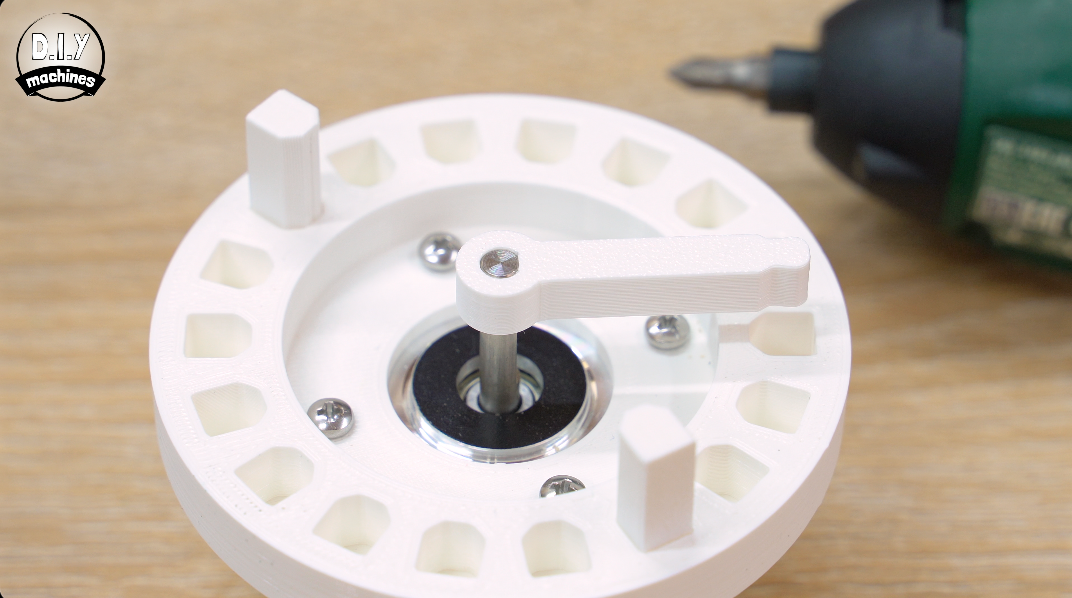 A 3D-printed white circular component with a central crank arm and gear-like teeth, sitting on a wooden surface.