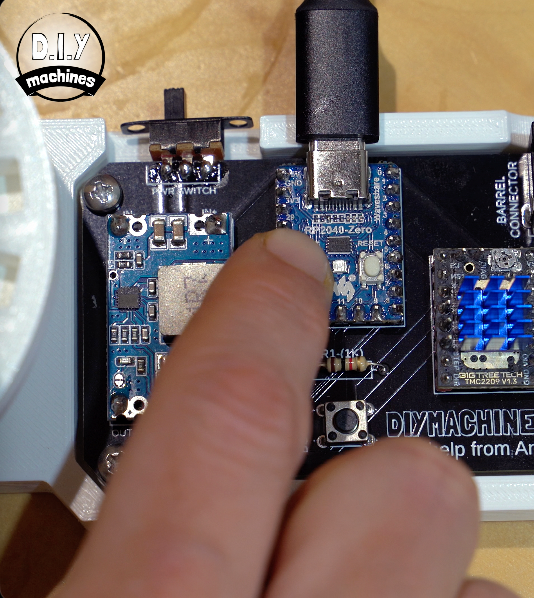 A finger presses a reset button on a blue Arduino Nano microcontroller mounted on a DIY electronics circuit board.
