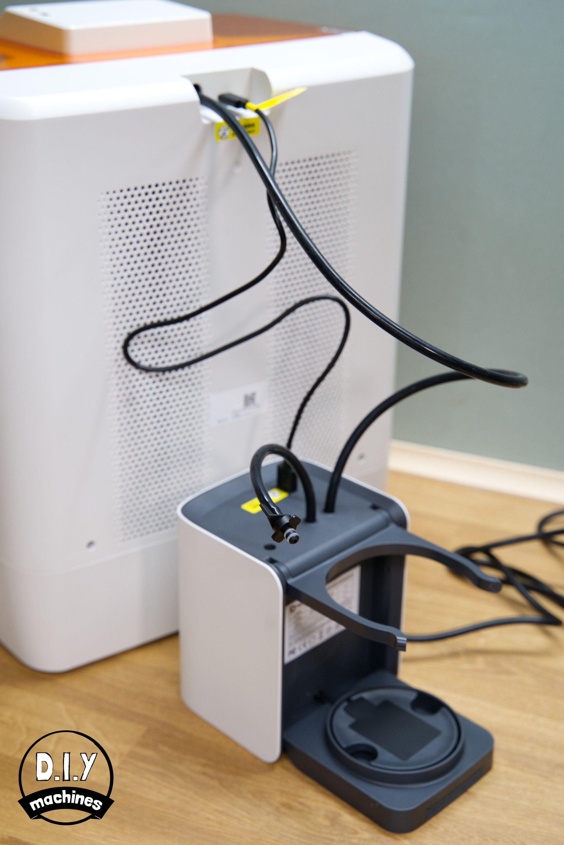 A white and gray printer-style device connected to a large white air purifier unit with black power and data cables.