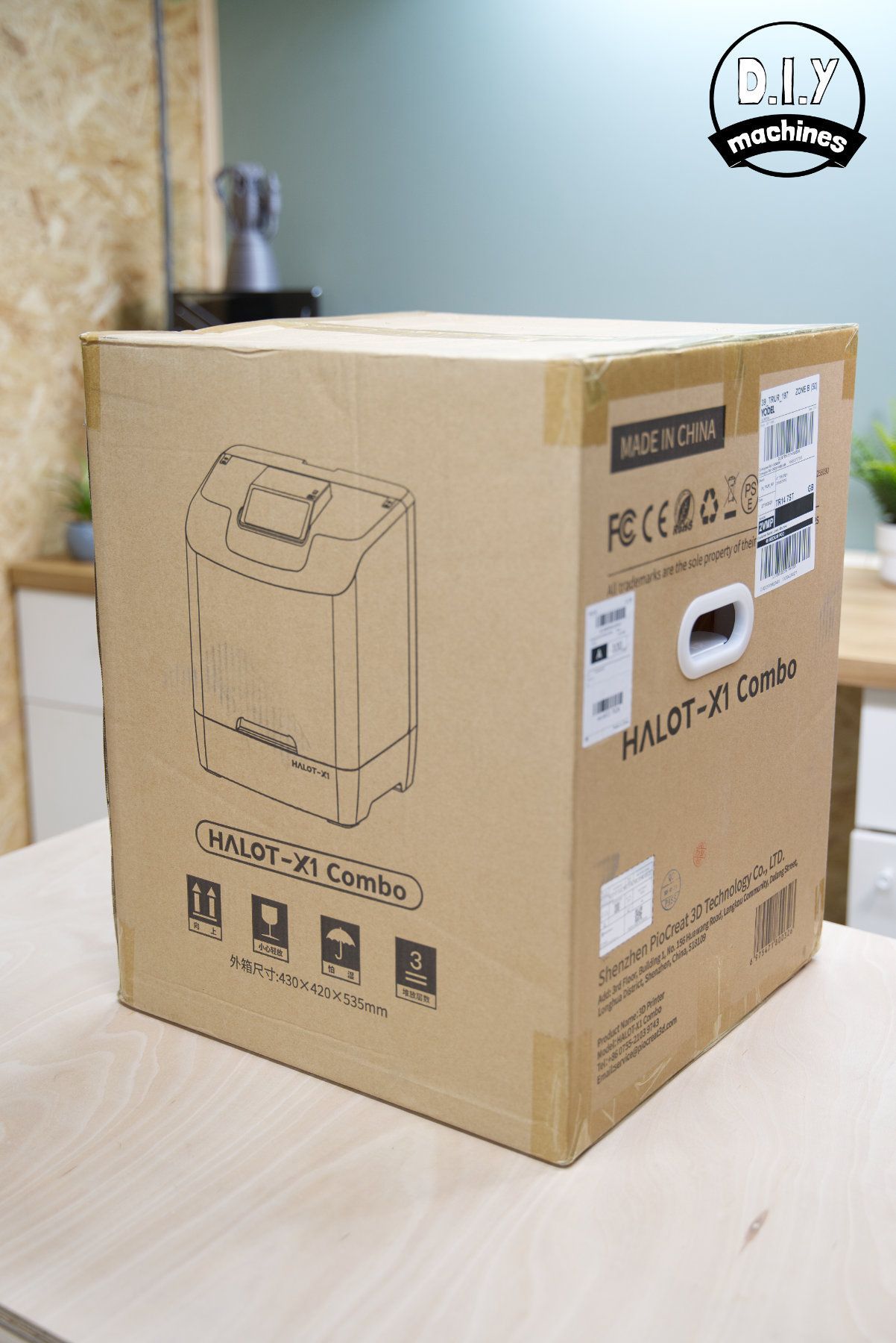 A cardboard box with a line-drawing illustration of a tall appliance, resting on a wooden surface in an office setting.
