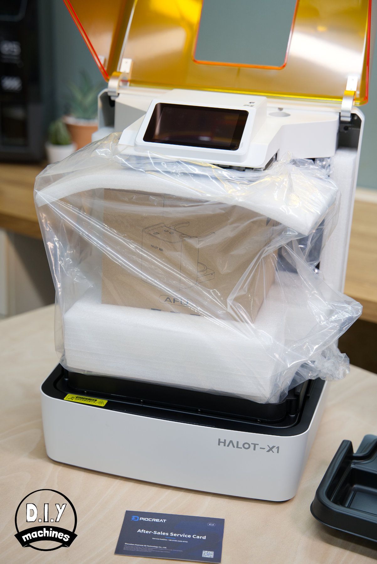 A Creality Halot-M1 resin 3D printer sits on a table, partially wrapped in protective plastic and foam packaging.