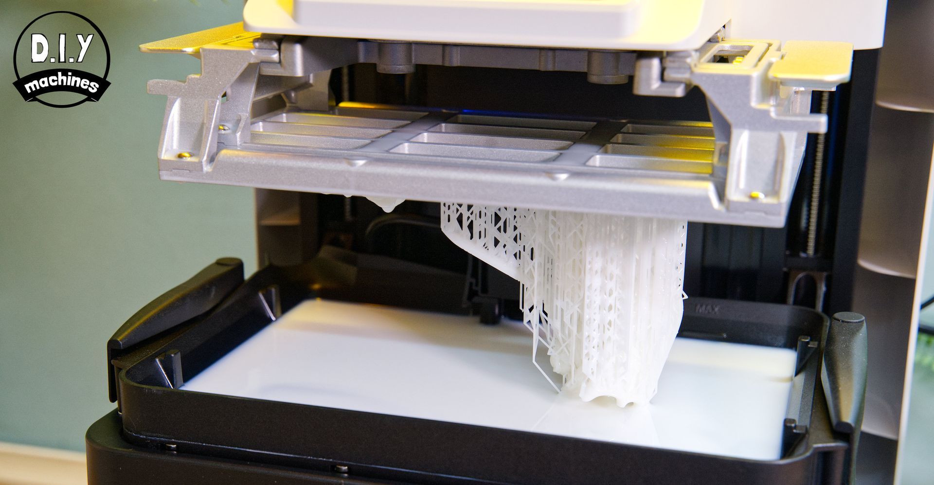 A 3D printer build plate lifting a white, complex lattice structure above a resin vat.